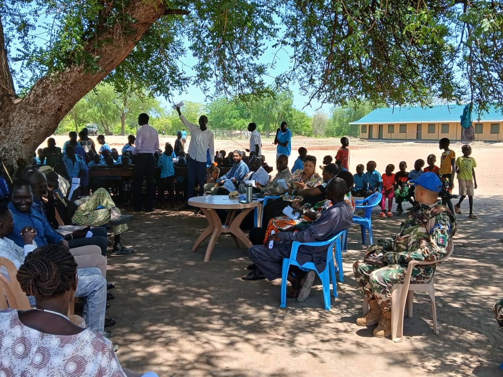 Community training session under tree with school building in background